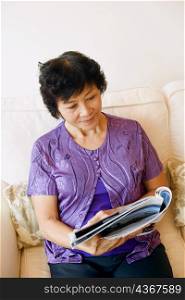 Mature woman sitting on a couch and reading a magazine