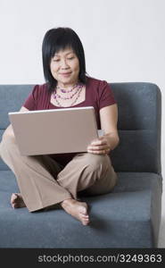 Mature woman sitting on a couch and using a laptop