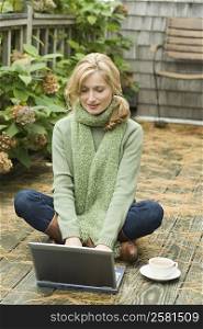 Mature woman sitting on a hardwood floor and using a laptop