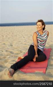 Mature woman sitting on a mat on the beach and smiling