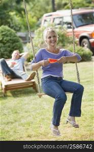 Mature woman sitting on a rope swing and holding a watermelon slice