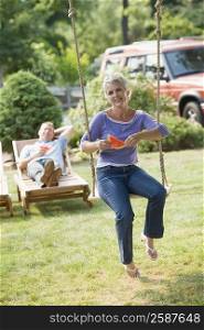 Mature woman sitting on a rope swing and holding a watermelon slice