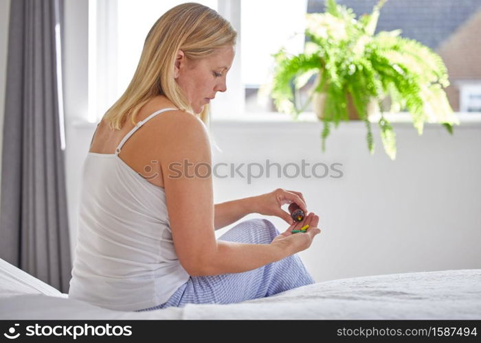 Mature Woman Sitting On Bed Wearing Pyjamas Taking Medication