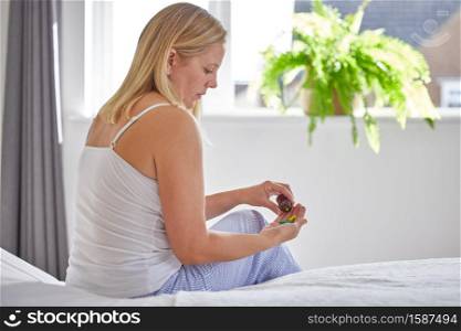 Mature Woman Sitting On Bed Wearing Pyjamas Taking Medication