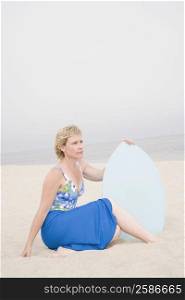 Mature woman sitting on the beach and holding a body board
