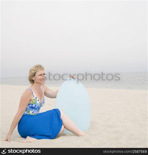 Mature woman sitting on the beach holding a body board and smiling