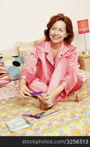 Mature woman sitting on the bed and filing her toenails with a nail file