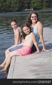 Mature woman sitting with her two daughters on the jetty and smiling
