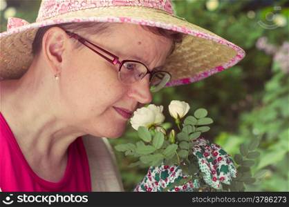 Mature woman sniffing the white rose in the garden, cross processed image