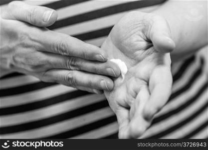 Mature woman spread out skincare cream to her hand, horizon format black and white image