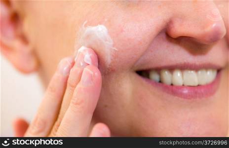 Mature woman spreading skincare cream on her cheek, horizon format
