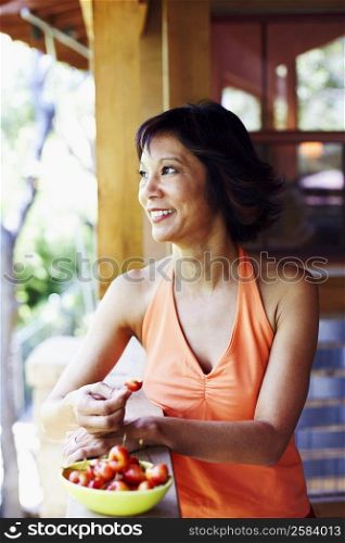 Mature woman standing in a balcony and eating cherries