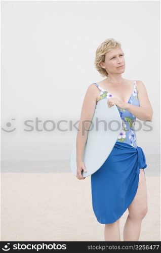 Mature woman standing on the beach and holding a body board