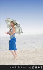 Mature woman standing on the beach and holding an umbrella