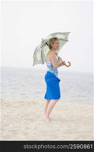 Mature woman standing on the beach and holding an umbrella