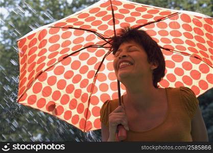 Mature woman standing under an umbrella in rain and smiling