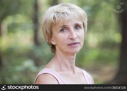 Mature woman stands in forest looking at camera