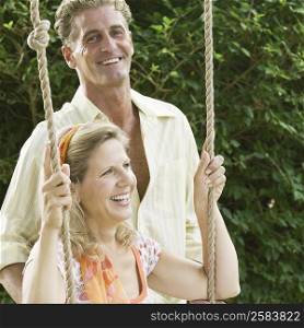 Mature woman swinging on a rope swing with a mature man standing beside him