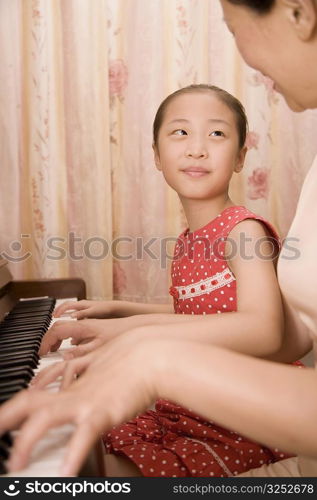 Mature woman teaching her granddaughter how to play a piano