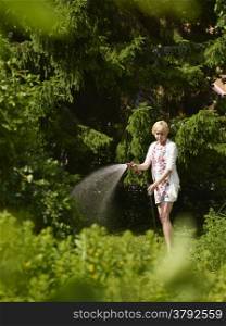 Mature woman use a garden hose, sunny summer day