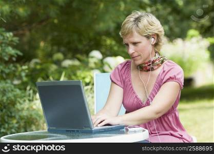Mature woman using a laptop and listening to an mp3 player