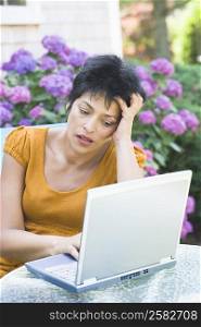 Mature woman using a laptop at an outdoor table and looking serious