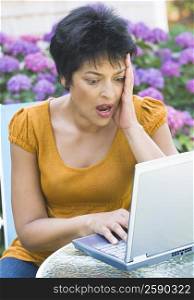 Mature woman using a laptop at an outdoor table and looking surprised