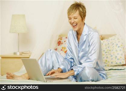 Mature woman using a laptop on the bed and laughing