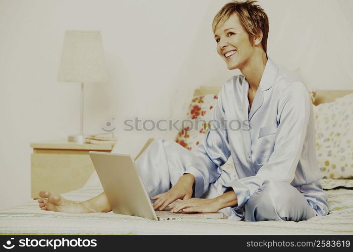 Mature woman using a laptop on the bed and smiling