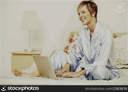 Mature woman using a laptop on the bed and smiling