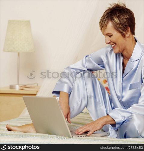 Mature woman using a laptop on the bed and smiling