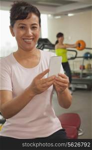 Mature woman using her cell phone in the gym, looking at the camera