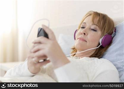 Mature woman using mobile phone while listening music at home