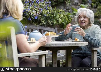 Mature Woman Visiting Lonely Senior Mother In Garden During Lockdown