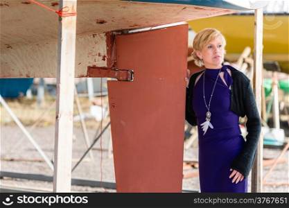 Mature woman wearing purple dress and posing, sailboat on background