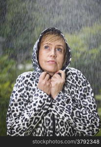 Mature woman wearing raincoat, rainy summer day, green nature on background