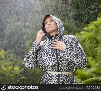 Mature woman wearing raincoat, rainy summer day, green nature on background