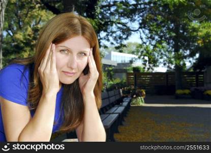 Mature woman with a headache sitting on the park bench