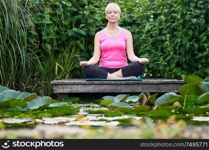 Mature Woman With Eyes Closed In Yoga Position On Wooden Jetty By Lake