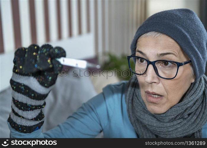 Mature woman with fever looking at Digital Thermometer for Body Temperature. Cold and Flu. Senior Woman Looking at Digital Thermometer