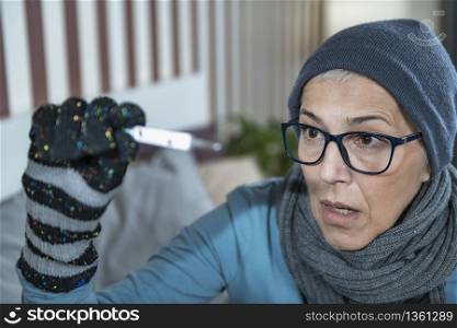 Mature woman with fever looking at Digital Thermometer for Body Temperature. Cold and Flu. Senior Woman Looking at Digital Thermometer