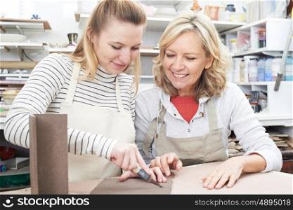 Mature Woman With Teacher Looking At Vase In Pottery Class