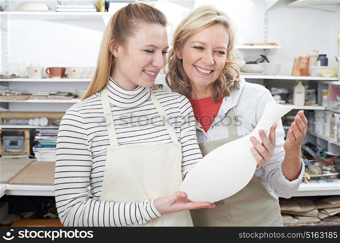 Mature Woman With Teacher Looking At Vase In Pottery Class