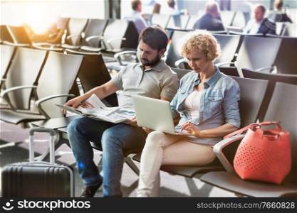 Mature woman working on her laptop,  husband is reading newspaper while waiting for boarding in airport