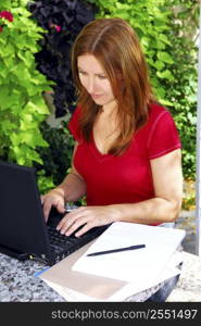 Mature woman working on portable computer in her garden at home