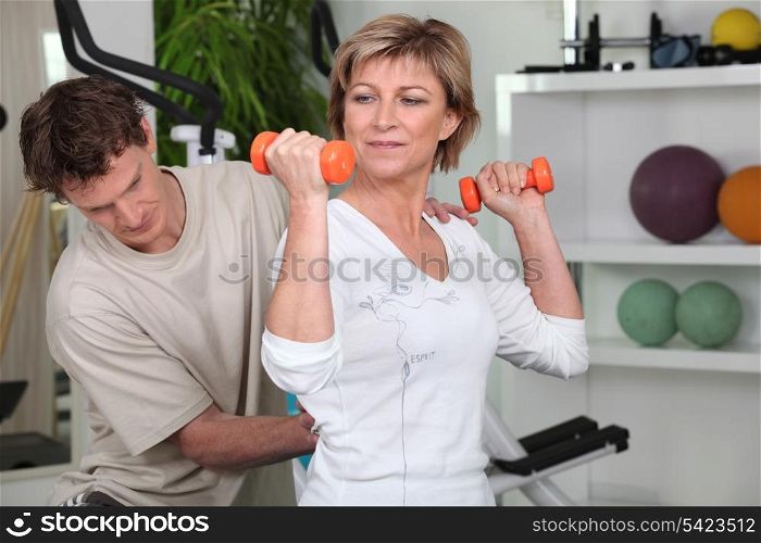 Mature woman working out with dumbbells and a personal trainer