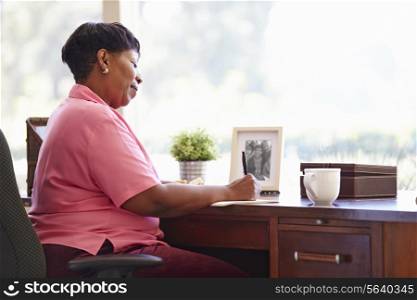 Mature Woman Writing In Notebook Sitting At Desk