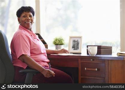 Mature Woman Writing In Notebook Sitting At Desk