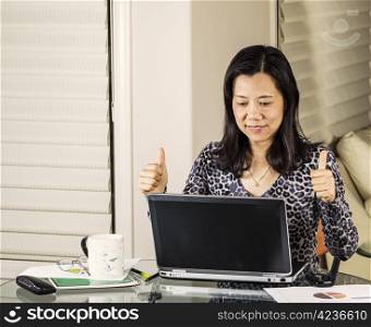 Mature women giving thumbs up on data results while working at home office