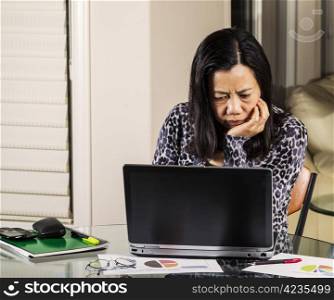 Mature women looking confused at information on computer while working from home